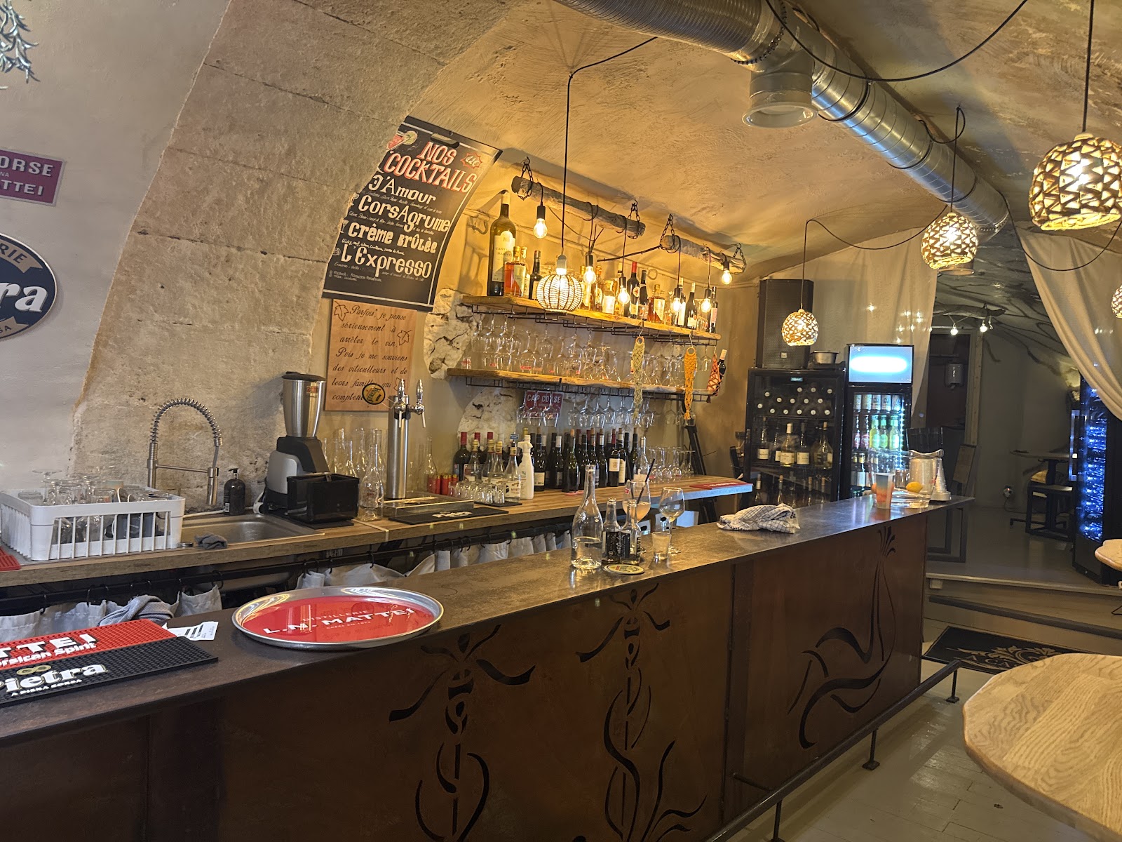 Le bar voûté en pierre, l'ardoise des cocktails et les suspensions tressées